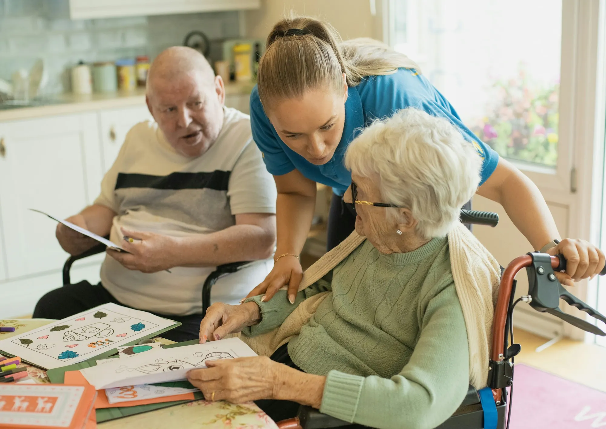 A caregiver sitting with two older women over a shared knitting project