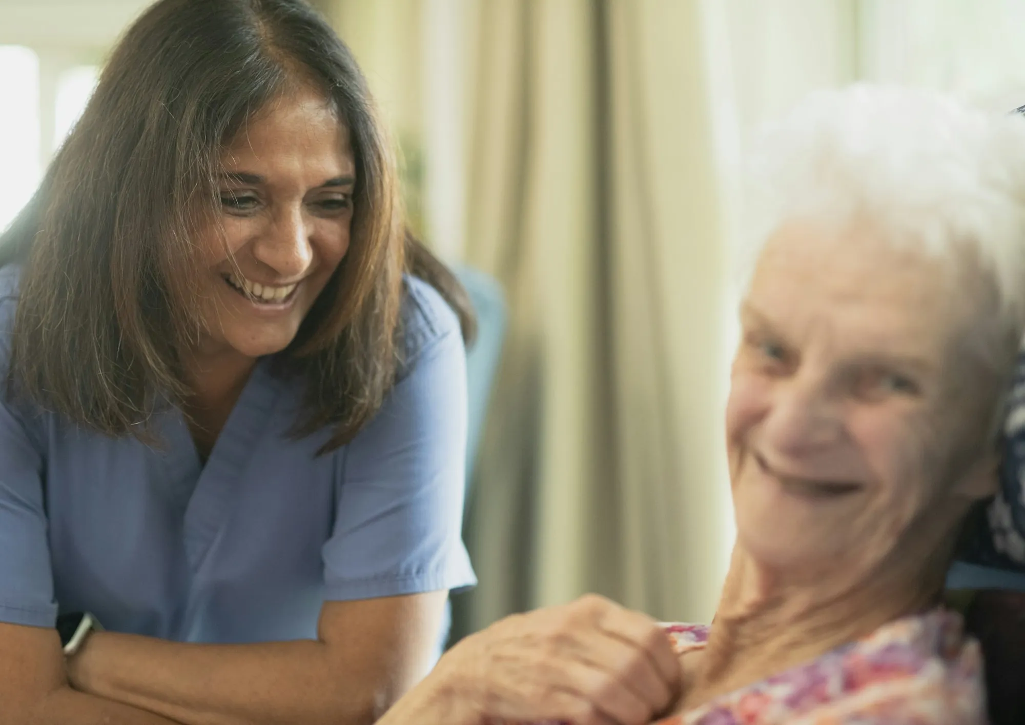 A care worker sitting and talking with an older woman in her own room