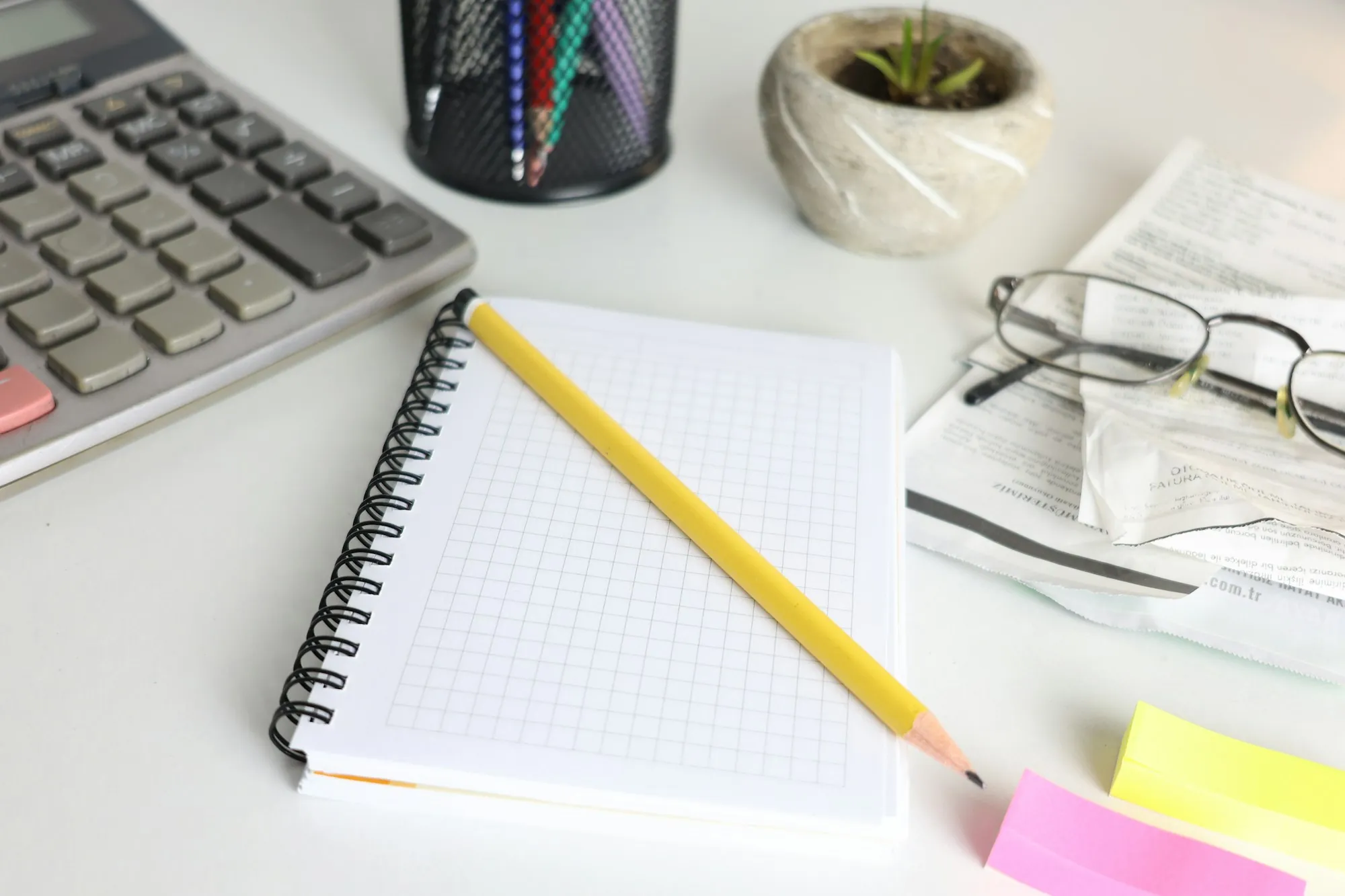 A tidy desk with a notebook, a pencil and a pair of reading glasses