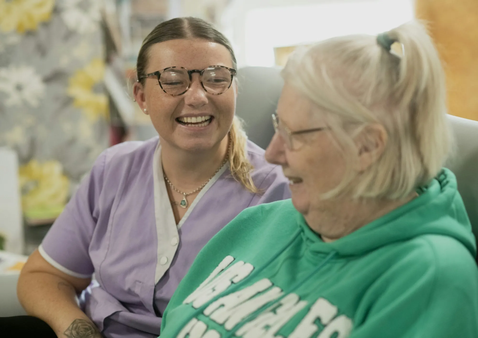 An aide standing with a group of older adults in a bright shared room